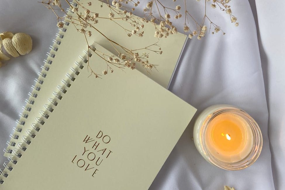 spiral notebooks placed on white cloth with burning candle